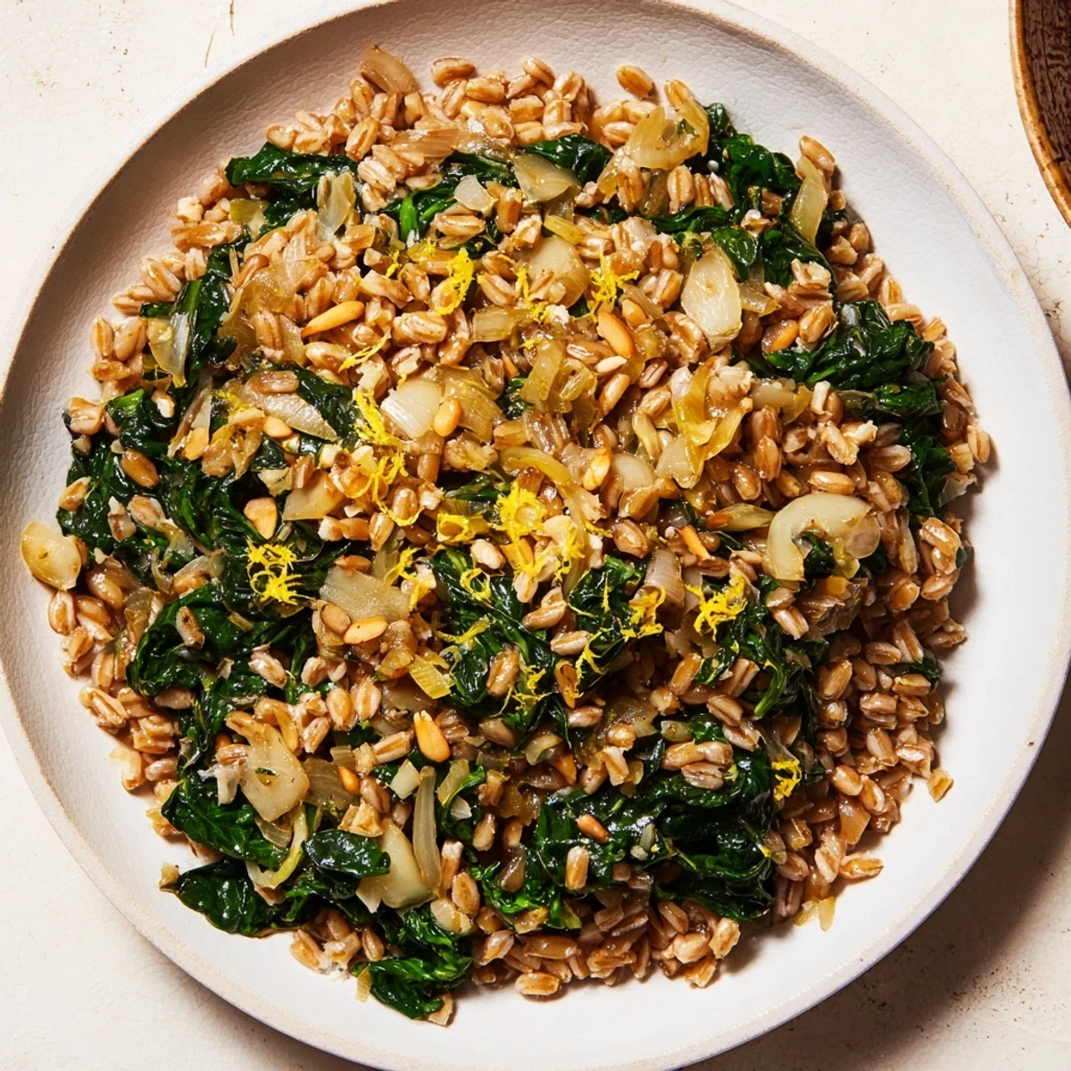 Steaming bowl of warm farro and greens pilaf, topped with toasted almonds, ready to serve.