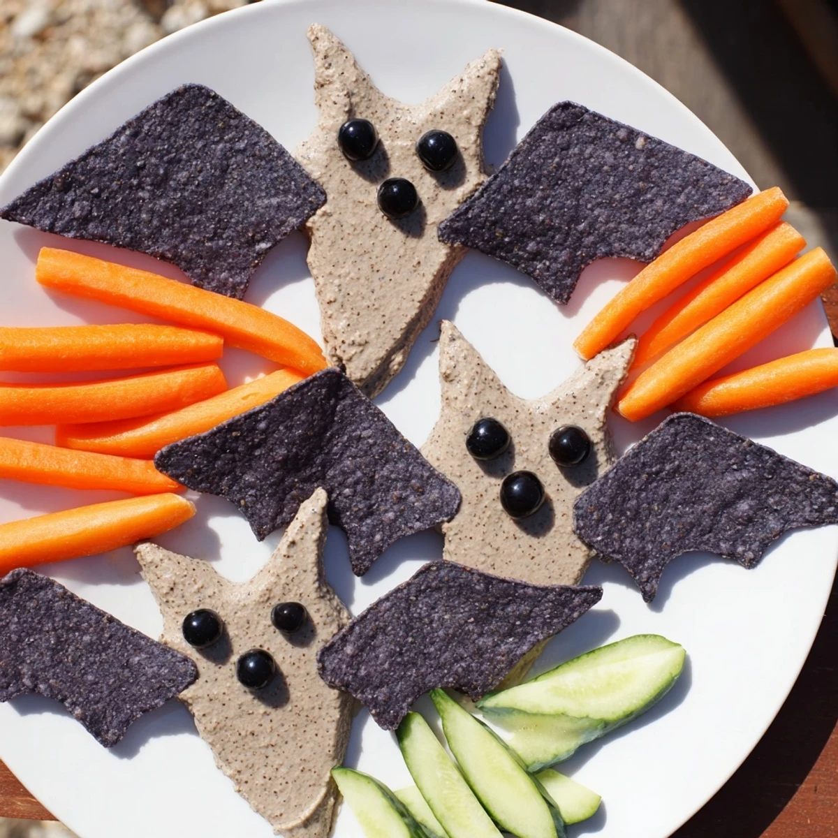 A creamy Spooky Bat Bean Dip Platter decorated with black olive eyes and colorful veggies.