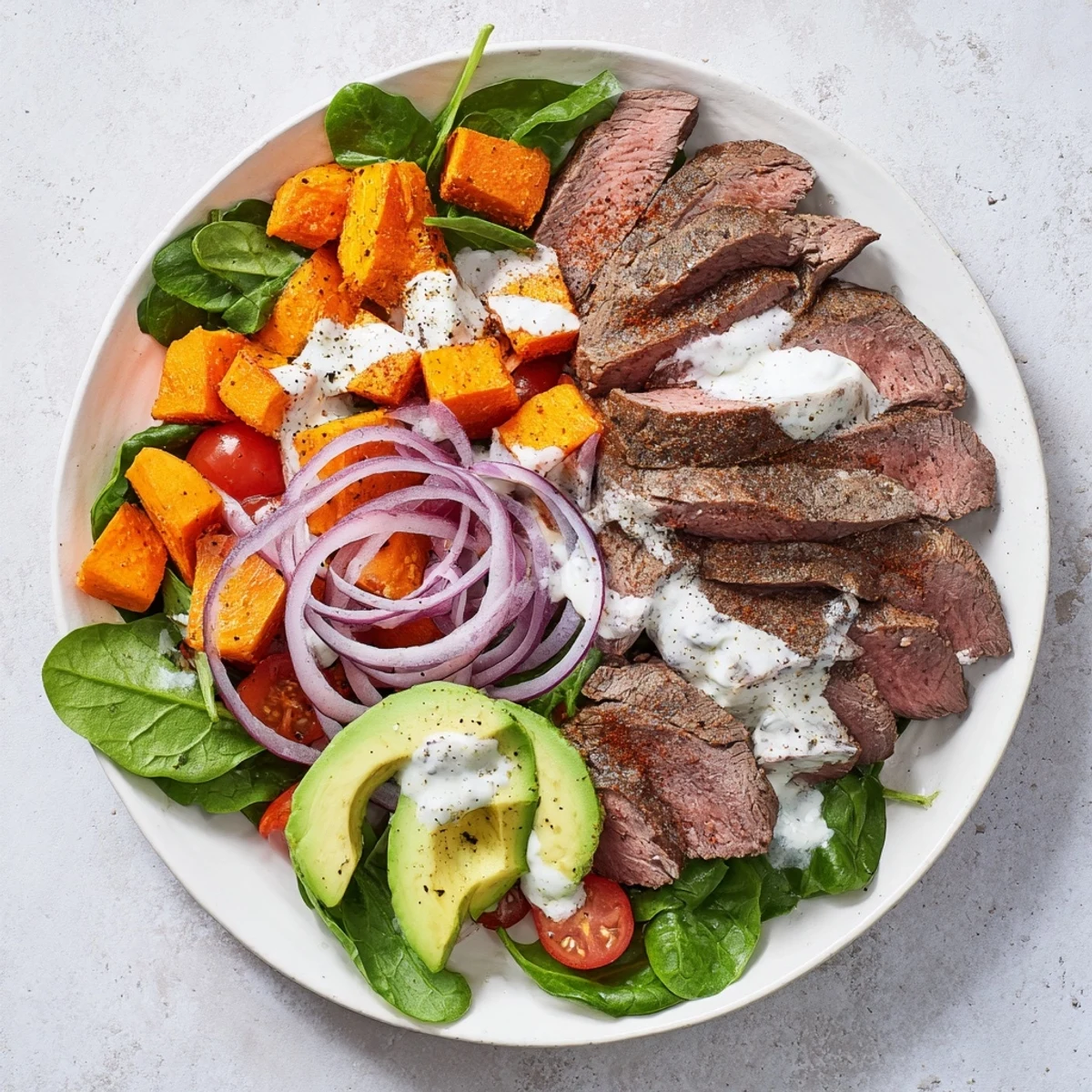 This colorful Beef Avocado Sweet Potato Bowl features seared beef with vibrant tomatoes and a creamy yogurt dressing.