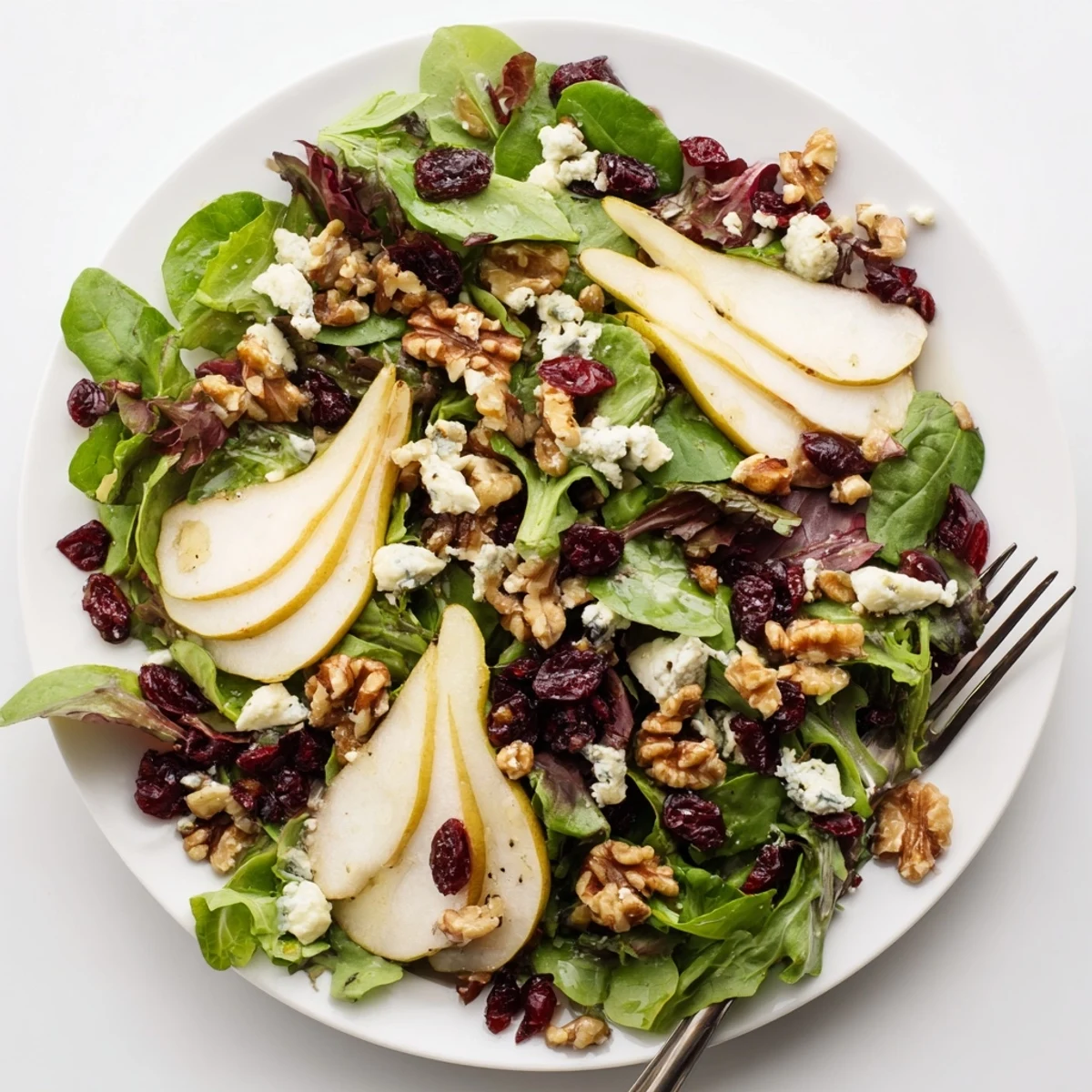 Pear Gorgonzola Salad arranged on a white plate, featuring juicy pear slices, blue cheese crumbles, toasted nuts, and greens for a light lunch.