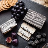 Dark, artfully arranged Monochrome Gray Stone Cheese Board, featuring crackers, olive tapenade, and fruit.