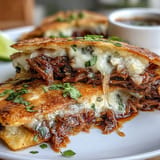 Crispy birria quesadillas with vibrant, savory consommé for dipping perfection.