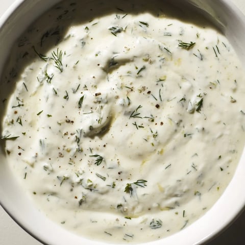 Creamy Greek Yogurt Ranch Dip boasts fresh herbs next to a platter of colorful, crunchy vegetables.