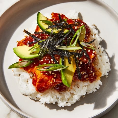 Emily Mariko-Inspired Sticky Orange Gochujang Salmon Bowl with glistening glaze and fresh cucumber slices on top.