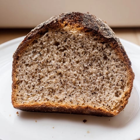 A golden-brown Latvian Rupjmaize bread loaf, speckled with caraway seeds, ready for slicing.
