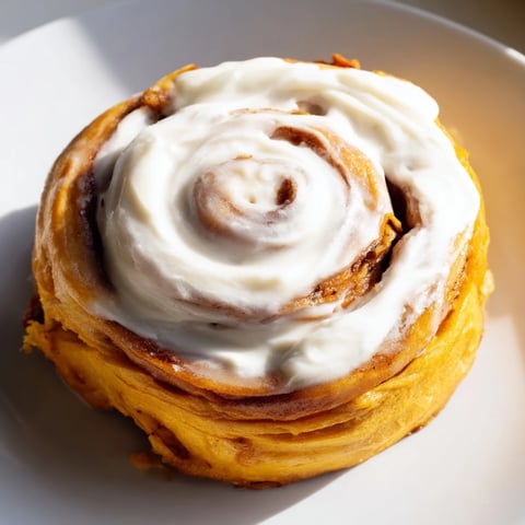 Golden-baked Pumpkin Cinnamon Rolls are arranged on a wooden board, their soft swirls glistening with a generous layer of cream cheese frosting.