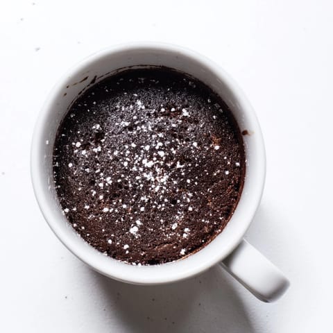 A warm, single-serving microwave mug cake, topped with a scoop of vanilla ice cream.
