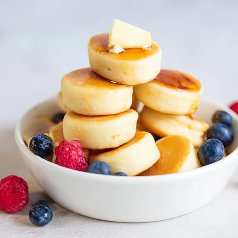 Miniature, perfectly cooked Pancake Cereal spilling from a bowl, ready for a delicious breakfast.