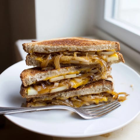 Close-up of a warm Caramelized Onion, Apple & Cheddar Grilled Cheese with oozing, melted cheddar cheese.