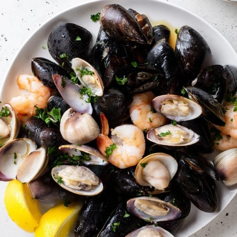 Steaming Shellfish & Seafood Medley overflowing with mussels, clams, shrimp, and herbs, ready to serve alongside lemon wedges.