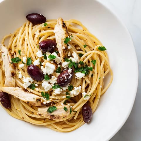 Plate of Greek Chicken Spaghetti topped with crumbled feta and parsley, served beside a glass of Assyrtiko wine.  