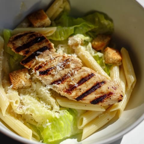 A close-up of Caesar Pasta Chicken Bowl featuring halved cherry tomatoes, garlic croutons, and freshly grated Parmesan cheese.