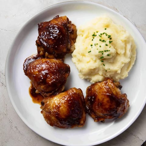 Golden-brown honey BBQ chicken thighs glistening, served with fluffy garlic mashed potatoes for dinner.