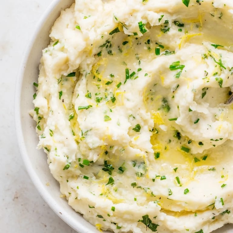 Close-up shot shows a fluffy, seasoned cauliflower mash topped with fresh herbs ready to eat.