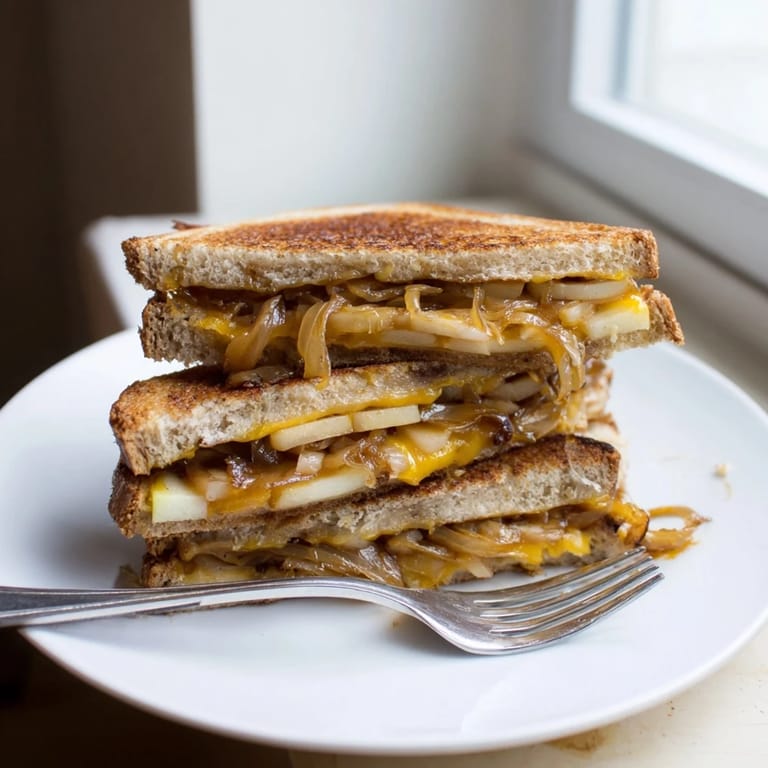Close-up of a warm Caramelized Onion, Apple & Cheddar Grilled Cheese with oozing, melted cheddar cheese.
