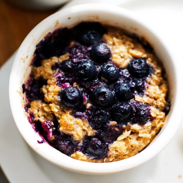 Fresh blueberries burst within golden, baked blueberry oats, perfect for a cozy brunch at home.