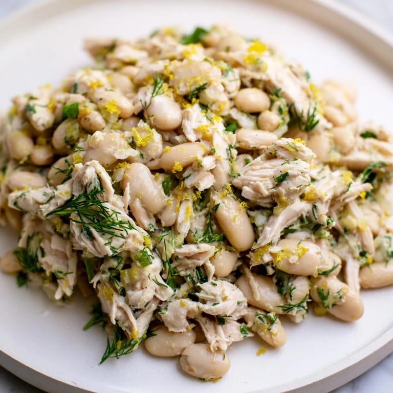 A bowl of Lemony White Bean Chicken Salad showcases juicy cherry tomatoes, red onion, and herbs, ready for a light lunch or summery main dish.  